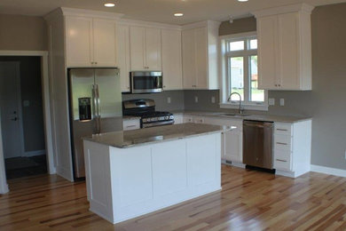 Eat-in kitchen - mid-sized traditional l-shaped light wood floor eat-in kitchen idea in Minneapolis with an undermount sink, recessed-panel cabinets, white cabinets, granite countertops, gray backsplash, stainless steel appliances and an island