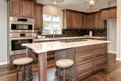 Example of a mid-sized transitional l-shaped dark wood floor and brown floor kitchen design in Sacramento with an undermount sink, raised-panel cabinets, dark wood cabinets, brown backsplash, glass tile backsplash, an island and beige countertops