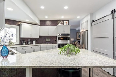 Mid-sized elegant u-shaped medium tone wood floor and gray floor eat-in kitchen photo in Miami with stainless steel appliances, an island, an undermount sink, flat-panel cabinets, gray cabinets, granite countertops, mosaic tile backsplash and gray countertops