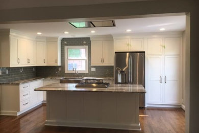 Inspiration for a medium tone wood floor and brown floor kitchen remodel in Louisville with a farmhouse sink, shaker cabinets, white cabinets, granite countertops, gray backsplash, subway tile backsplash and stainless steel appliances