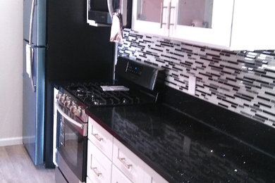 ロサンゼルスにある中くらいなトランジショナルスタイルのおしゃれなI型キッチン (シェーカースタイル扉のキャビネット、白いキャビネット、御影石カウンター、マルチカラーのキッチンパネル、アイランドなし、茶色い床、黒いキッチンカウンター) の写真