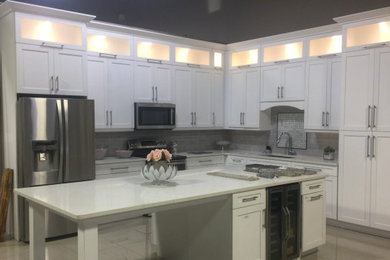 Mid-sized trendy kitchen photo in Tampa with recessed-panel cabinets, white cabinets, gray backsplash, stainless steel appliances, an island and white countertops
