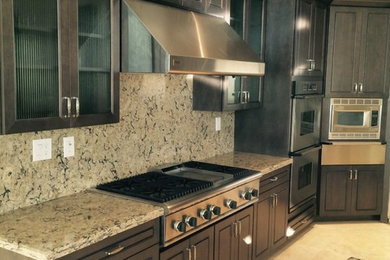 Inspiration for a large transitional l-shaped ceramic tile and beige floor kitchen remodel in Phoenix with a double-bowl sink, granite countertops, multicolored backsplash, stone slab backsplash, stainless steel appliances, raised-panel cabinets, dark wood cabinets and an island