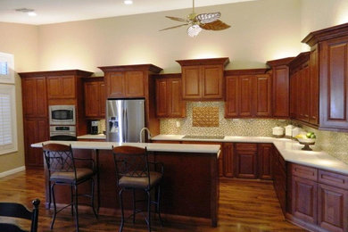 Example of a mid-sized classic l-shaped medium tone wood floor and brown floor open concept kitchen design in Phoenix with an undermount sink, raised-panel cabinets, medium tone wood cabinets, quartzite countertops, beige backsplash, ceramic backsplash, stainless steel appliances and an island