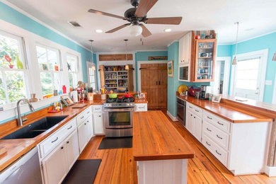 Example of a mid-sized eclectic u-shaped medium tone wood floor and beige floor open concept kitchen design in Atlanta with a double-bowl sink, recessed-panel cabinets, white cabinets, wood countertops, brown backsplash, wood backsplash, stainless steel appliances and an island
