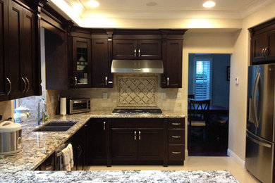 Example of a mid-sized trendy u-shaped linoleum floor and beige floor enclosed kitchen design in Orange County with a double-bowl sink, recessed-panel cabinets, dark wood cabinets, granite countertops, beige backsplash, stone tile backsplash, stainless steel appliances and a peninsula