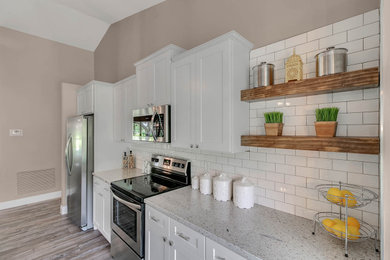 Inspiration for a mid-sized country single-wall laminate floor and gray floor open concept kitchen remodel in Orlando with an undermount sink, shaker cabinets, white cabinets, granite countertops, white backsplash, subway tile backsplash, stainless steel appliances, an island and gray countertops