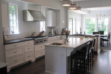 Kitchen - large traditional l-shaped dark wood floor kitchen idea in Newark with white backsplash, subway tile backsplash, stainless steel appliances, an undermount sink, flat-panel cabinets, white cabinets, soapstone countertops and an island
