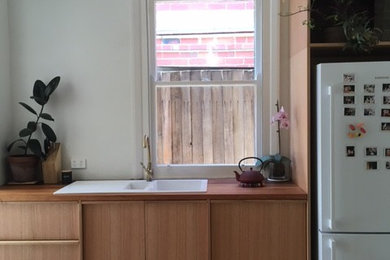 Inredning av ett modernt litet linjärt kök och matrum, med en dubbel diskho, släta luckor, skåp i ljust trä, träbänkskiva, vitt stänkskydd, vita vitvaror och ljust trägolv