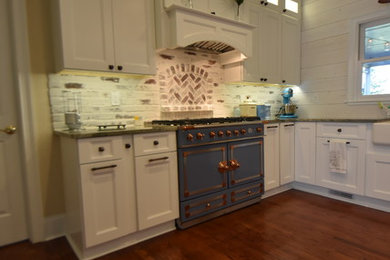 Example of a mid-sized country u-shaped medium tone wood floor and brown floor eat-in kitchen design in Atlanta with a farmhouse sink, flat-panel cabinets, white cabinets, granite countertops, multicolored backsplash, brick backsplash, colored appliances, a peninsula and green countertops