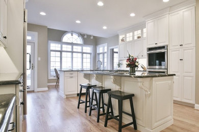 Eat-in kitchen - large traditional light wood floor eat-in kitchen idea in Philadelphia with glass-front cabinets, white cabinets, granite countertops, white backsplash, ceramic backsplash, stainless steel appliances and two islands