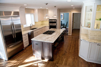 Inspiration for a large timeless u-shaped medium tone wood floor eat-in kitchen remodel in Detroit with an undermount sink, glass-front cabinets, white cabinets, granite countertops, beige backsplash, stone tile backsplash, stainless steel appliances and an island