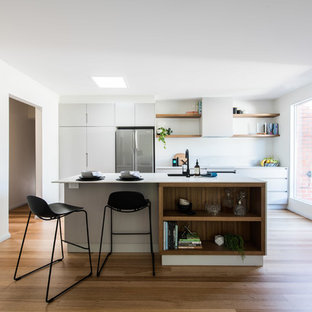 This is an example of a mid-sized contemporary galley kitchen in Melbourne with medium hardwood floors, with island, white benchtop, an undermount sink, flat-panel cabinets, white cabinets, white splashback, stainless steel appliances and brown floor.