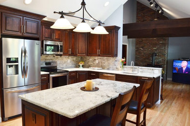 Mid-sized transitional l-shaped light wood floor eat-in kitchen photo in New York with an undermount sink, raised-panel cabinets, dark wood cabinets, quartzite countertops, gray backsplash, stone tile backsplash, stainless steel appliances and an island