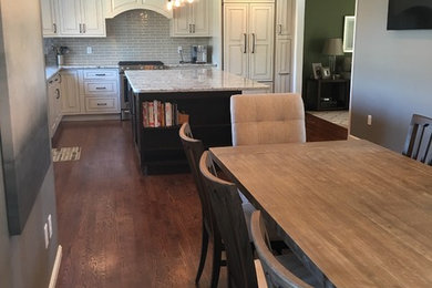 Mid-sized elegant l-shaped dark wood floor eat-in kitchen photo in Cincinnati with an undermount sink, beaded inset cabinets, white cabinets, granite countertops, gray backsplash, glass tile backsplash, paneled appliances and an island