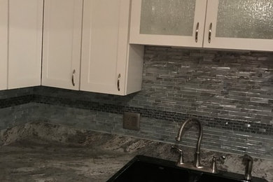 Example of a mid-sized transitional l-shaped kitchen design in New York with a drop-in sink, shaker cabinets, white cabinets, granite countertops, gray backsplash, matchstick tile backsplash and stainless steel appliances
