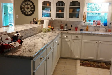Example of a mid-sized classic l-shaped ceramic tile kitchen design in Houston with a drop-in sink, shaker cabinets, white cabinets, granite countertops, stone tile backsplash, white appliances and a peninsula