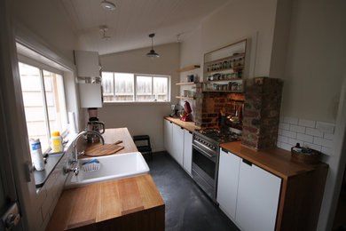 メルボルンにある小さな北欧スタイルのおしゃれなキッチン (エプロンフロントシンク、フラットパネル扉のキャビネット、白いキャビネット、木材カウンター、白いキッチンパネル、セラミックタイルのキッチンパネル、シルバーの調理設備、コンクリートの床、アイランドなし) の写真