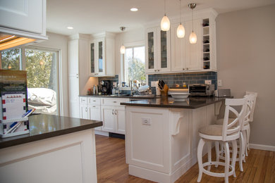 Inspiration for a mid-sized contemporary l-shaped medium tone wood floor and brown floor eat-in kitchen remodel in New York with recessed-panel cabinets, white cabinets, blue backsplash, subway tile backsplash, stainless steel appliances, a peninsula, an undermount sink and solid surface countertops