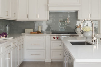 Inspiration for a large transitional l-shaped porcelain tile and beige floor open concept kitchen remodel in New York with an undermount sink, shaker cabinets, white cabinets, quartz countertops, gray backsplash, ceramic backsplash, stainless steel appliances, an island and beige countertops