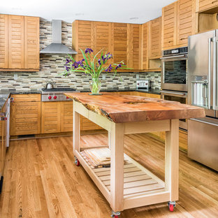 Photo of a tropical u-shaped kitchen in Richmond with an undermount sink, louvered cabinets, medium wood cabinets, multi-coloured splashback, matchstick tile splashback, stainless steel appliances, medium hardwood floors, with island, brown floor and black benchtop.