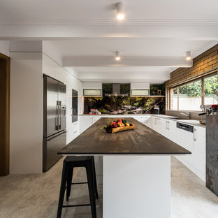 Photo of an industrial u-shaped kitchen in Melbourne with a single-bowl sink, flat-panel cabinets, white cabinets, black splashback, stone slab splashback, stainless steel appliances, with island, grey floor and black benchtop.