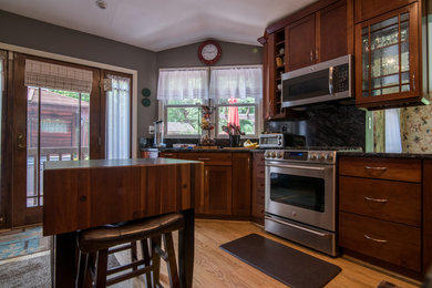 Foto på ett mellanstort vintage kök, med luckor med infälld panel, skåp i mellenmörkt trä, granitbänkskiva, grönt stänkskydd, stänkskydd i sten, rostfria vitvaror och ljust trägolv