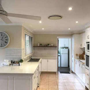 Inspiration for a mid-sized country u-shaped eat-in kitchen in Sydney with a double-bowl sink, shaker cabinets, white cabinets, quartzite benchtops, grey splashback, white appliances, no island and pink floor.