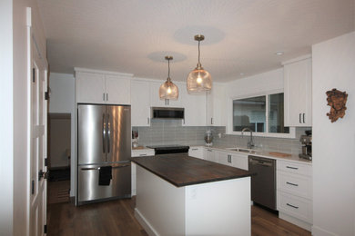 Example of a mid-sized minimalist l-shaped medium tone wood floor eat-in kitchen design in Other with shaker cabinets, white cabinets, gray backsplash, stainless steel appliances and an island