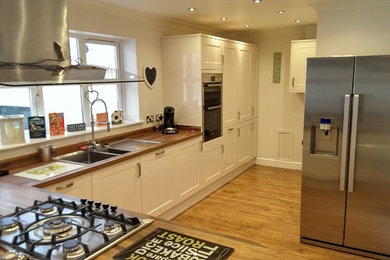 Medium sized contemporary l-shaped kitchen/diner in Other with a double-bowl sink, shaker cabinets, light wood cabinets, wood worktops, stainless steel appliances, light hardwood flooring and an island.