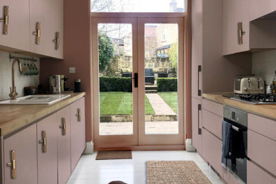 Design ideas for a medium sized contemporary galley enclosed kitchen in London with a built-in sink, flat-panel cabinets, pink cabinets, wood worktops, white splashback, ceramic splashback, stainless steel appliances, painted wood flooring, no island, white floors and beige worktops.