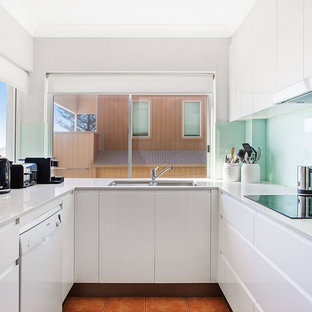 Small modern u-shaped kitchen in Gold Coast - Tweed with an undermount sink, flat-panel cabinets, white cabinets, glass sheet splashback, orange floor and grey benchtop.