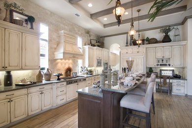 Example of a huge tuscan l-shaped light wood floor and brown floor eat-in kitchen design in New York with a drop-in sink, distressed cabinets, granite countertops, white backsplash, stainless steel appliances, two islands, raised-panel cabinets and stone tile backsplash