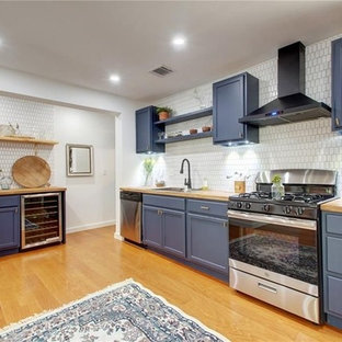Design ideas for a mid-sized country l-shaped eat-in kitchen in Austin with a single-bowl sink, louvered cabinets, blue cabinets, wood benchtops, white splashback, ceramic splashback, stainless steel appliances, laminate floors, no island, brown floor and brown benchtop.