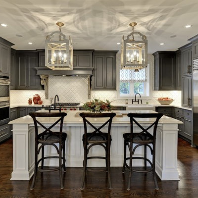 Large transitional u-shaped dark wood floor and brown floor kitchen photo in Minneapolis with gray cabinets, white backsplash, stainless steel appliances, an island, raised-panel cabinets, a farmhouse sink, solid surface countertops, white countertops and ceramic backsplash