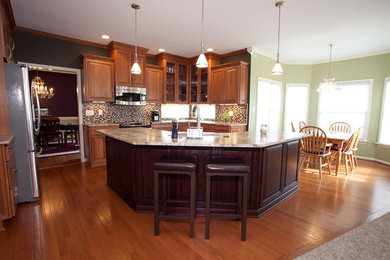 Modern inredning av ett stort kök, med en integrerad diskho, luckor med upphöjd panel, skåp i mellenmörkt trä, granitbänkskiva, svart stänkskydd, stänkskydd i glaskakel, rostfria vitvaror, mellanmörkt trägolv och en köksö