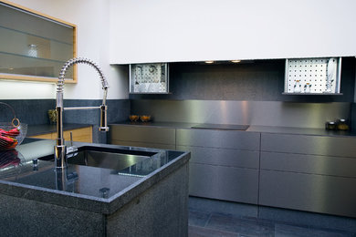 Photo of a small modern u-shaped kitchen/diner in Other with a belfast sink, flat-panel cabinets, light wood cabinets, granite worktops, grey splashback, stone tiled splashback, stainless steel appliances, marble flooring and an island.