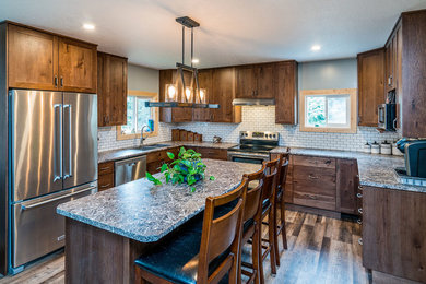 Mid-sized mountain style u-shaped medium tone wood floor and brown floor eat-in kitchen photo in Other with a drop-in sink, recessed-panel cabinets, medium tone wood cabinets, laminate countertops, white backsplash, subway tile backsplash, stainless steel appliances, an island and multicolored countertops