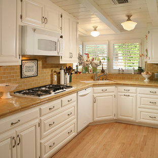 Photo of a traditional separate kitchen in Los Angeles with tile benchtops, white appliances, raised-panel cabinets, white cabinets, brown splashback and subway tile splashback.