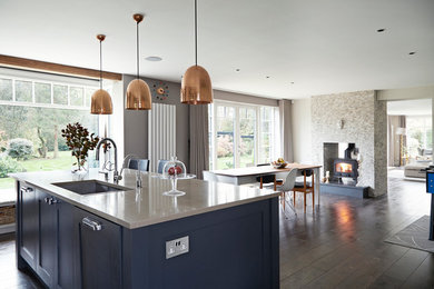 This is an example of a large contemporary single-wall open plan kitchen in Hertfordshire with a submerged sink, shaker cabinets, grey cabinets, composite countertops, metallic splashback, mirror splashback, integrated appliances, dark hardwood flooring, an island, brown floors and grey worktops.