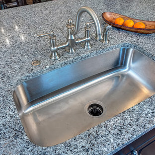 Ejemplo de cocina en U, grande, abierta, con fregadero bajoencimera, armarios con paneles con relieve, puertas de armario beige, encimera de granito, salpicadero blanco, salpicadero de azulejos tipo metro, electrodomésticos de acero inoxidable, suelo de madera en tonos medios y una isla