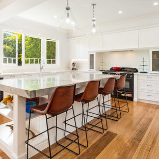 Inspiration for a mid-sized transitional u-shaped kitchen in Sydney with a farmhouse sink, shaker cabinets, white cabinets, white splashback, subway tile splashback, black appliances, medium hardwood floors, with island, brown floor and beige benchtop.