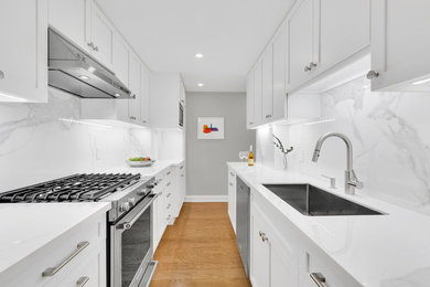 Enclosed kitchen - mid-sized modern galley light wood floor and beige floor enclosed kitchen idea in New York with a drop-in sink, recessed-panel cabinets, white cabinets, multicolored backsplash, stainless steel appliances, quartz countertops, stone slab backsplash and white countertops