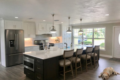 Open concept kitchen - large traditional single-wall brown floor and vinyl floor open concept kitchen idea in Orlando with white backsplash, stainless steel appliances, an island, white countertops, shaker cabinets, white cabinets, quartz countertops and a farmhouse sink