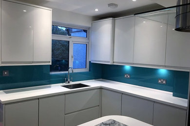Inspiration for a contemporary kitchen in London with blue splashback, glass sheet splashback and white appliances.