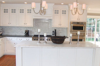 Example of a mid-sized classic l-shaped light wood floor and beige floor eat-in kitchen design in Philadelphia with raised-panel cabinets, white cabinets, solid surface countertops, white backsplash, matchstick tile backsplash, stainless steel appliances and an island