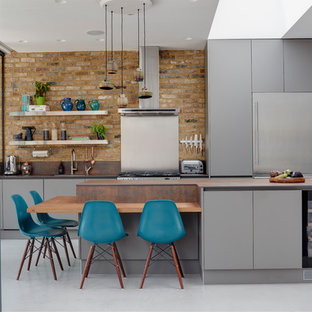 Large contemporary kitchen in London with flat-panel cabinets, grey cabinets, composite countertops, stainless steel appliances, concrete flooring, an island, grey floors, brown worktops, a single-bowl sink and brick splashback.