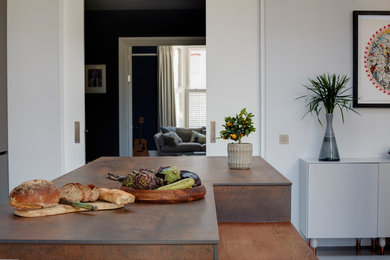 Bild på ett stort funkis brun linjärt brunt kök med öppen planlösning, med en integrerad diskho, släta luckor, grå skåp, bänkskiva i koppar, brunt stänkskydd, stänkskydd i porslinskakel, rostfria vitvaror, betonggolv, en köksö och grått golv