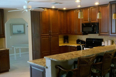 Elegant u-shaped eat-in kitchen photo in Miami with an undermount sink, raised-panel cabinets, dark wood cabinets, granite countertops, beige backsplash and black appliances