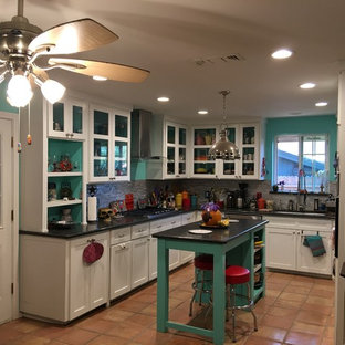 Mid-sized eclectic u-shaped open plan kitchen in Dallas with an undermount sink, glass-front cabinets, white cabinets, granite benchtops, grey splashback, glass tile splashback, stainless steel appliances, terra-cotta floors, with island and beige floor.